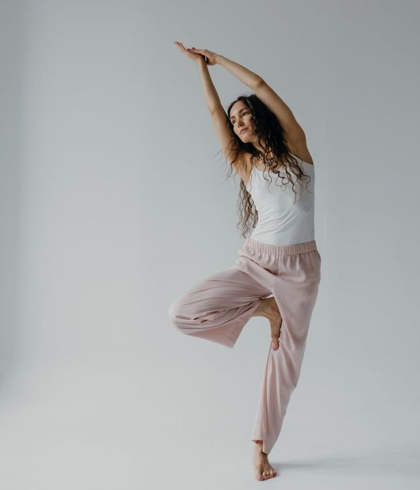 Person in a calm, flowing movement pose in a minimalist studio environment.